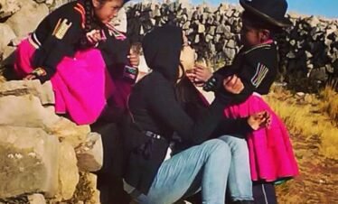 Girls in Luquina Chico traditional attire engaging with a tourist by Lake Titicaca in Puno, Peru