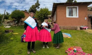 Local mother helping visitors wear colorful Aymara clothing in Luquina Chico by Lake Titicaca Puno Peru