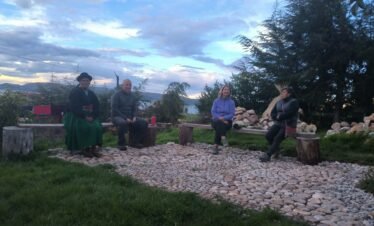 Travelers sharing conversation with local host in traditional courtyard of Luquina Chico guesthouse by Lake Titicaca Puno Peru