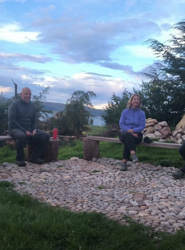 Travelers sharing conversation with local host in traditional courtyard of Luquina Chico guesthouse by Lake Titicaca Puno Peru