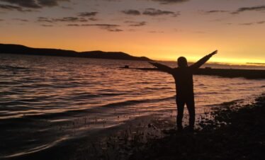 First light of dawn reflecting on calm waters of Lake Titicaca with Luquina Chico in Puno Peru
